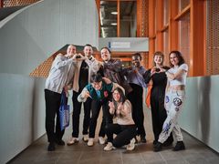 Ryhmä ihmisiä seisoo käytävällä ja poseeraa yhdessä iloisesti, osa tekee käsillään sydämen.