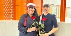 Two smiling graduates holding roses and wearing traditional caps at Vaasa University of Applied Sciences.
