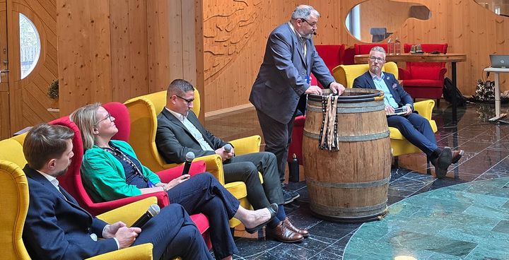 A group of five people sits and stands around a wooden barrel, engaging in a discussion during a seminar.