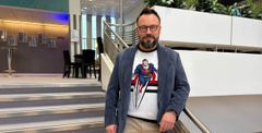 Riku Rantala seisoo portaikon vierellä sisätiloissa. Hänellä on sininen bleiseri Superman-aiheisen t-paidan päällä ja beigit housut.