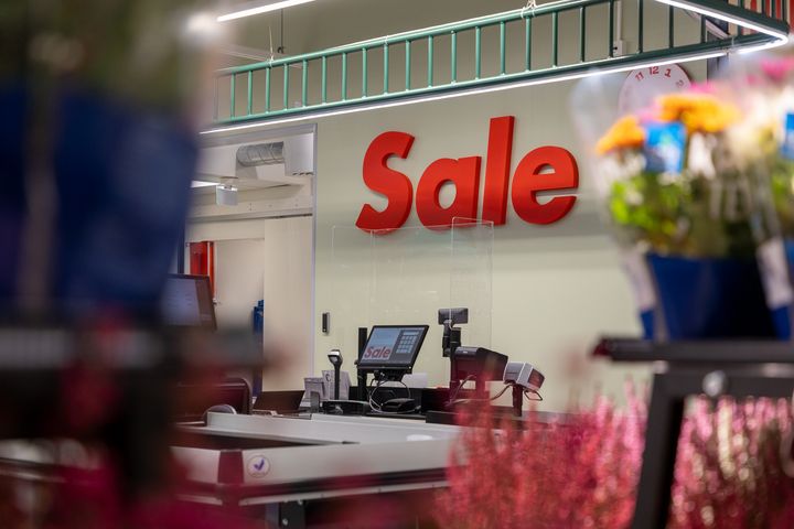 Myymälän kassa-alue, jossa näkyy Sale-kyltti ja kukkia etualalla.
