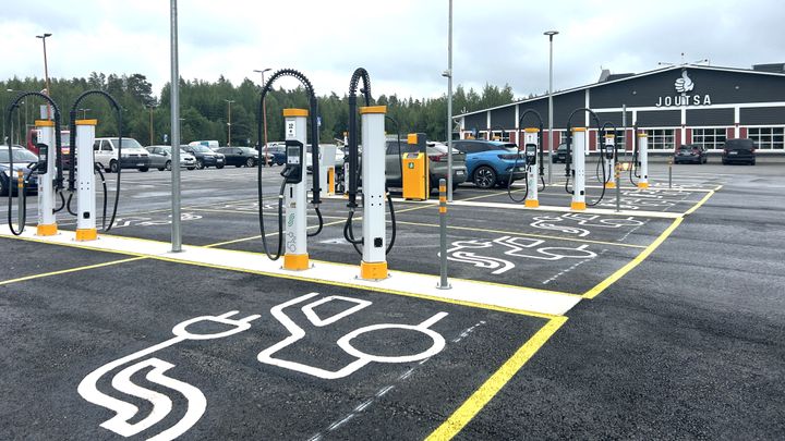 Kuva Joutsan ABC:stä, jossa on useita sähköautojen latauspisteitä päivitetyllä latausasemalla. Taustalla näkyy Joutsan ABC-liikennemyymälä.