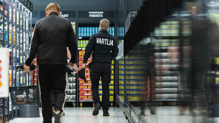 Kaksi ihmistä kaupan käytävällä, toinen on vartija.