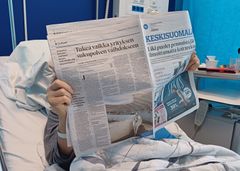 Henkilö lukee sanomalehteä sairaalasängyssä.