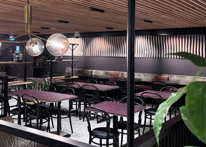 Näkymä modernista ja viihtyisästä ravintolatilasta, jossa on puisia elementtejä, mukavia tuoleja ja useita pöytiä.