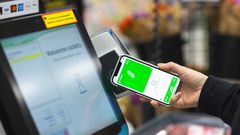 Käsi pitää puhelinta maksupäätteen lähellä kaupan kassalla. Näytöllä näkyy sovellus, jossa on vihreä tausta ja S-Etukortin kuva.
