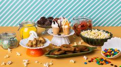 Jälkiruokapöytä täynnä värikkäitä herkkuja, kuten karkkeja, jäätelöannoksia, popcorneja ja leivonnaisia.