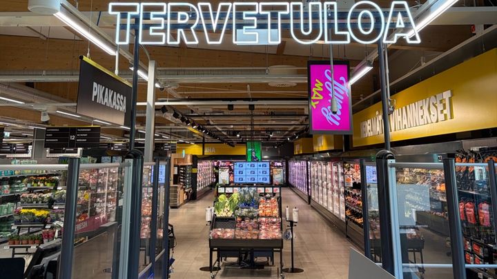 Alt-teksti: S-market Hankasalmen sisäänkäynti, jossa näkyy kylmälaitteita ja valikoimaa täynnä olevia hyllyjä. Katossa lukee "Tervetuloa".