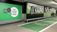 Alt-teksti: Prisman noutopiste parkkihallissa, jossa on vihreitä opasteita ja mainoksia verkkokaupan käytöstä.