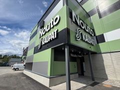 Alt-teksti: Vihreä ja harmaa rakennus, jossa näkyy "Nouto Kaupat" -kyltti.