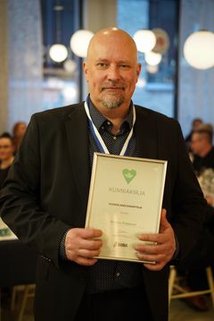 Mies hymyilee ja pitelee kunniakirjaa.