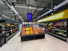 Kuva supermarketin hedelmä- ja vihannesosastosta, jossa on erilaisia hedelmiä ja vihanneksia esillä.