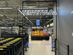 Ruokakaupan sisäänkäynti, jossa on hedelmäosasto ja tervetuloteksti.