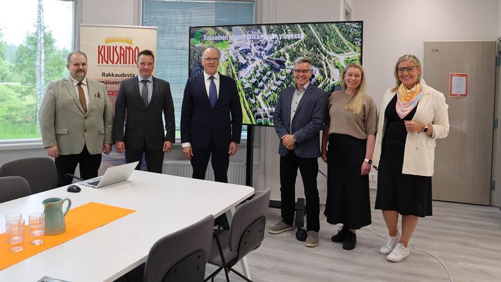 Ryhmä ihmisiä seisoo neuvotteluhuoneessa ison näytön edessä.