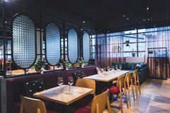 Moderni ravintolasali, jossa on puisia pöytiä, viinilaseja ja kasveja koristeina.