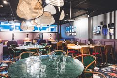 Ravintolasali, jossa on pyöreitä pöytiä ja punaisia sekä puunvärisiä tuoleja. Katossa roikkuvia koristeellisia valaisimia.