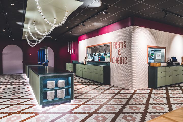 Ravintolasisustus, jossa on modernit vihreät tiskit, koristevalaistus ja kuvioitu lattia. Seinällä lukee "Frans & Cherie".