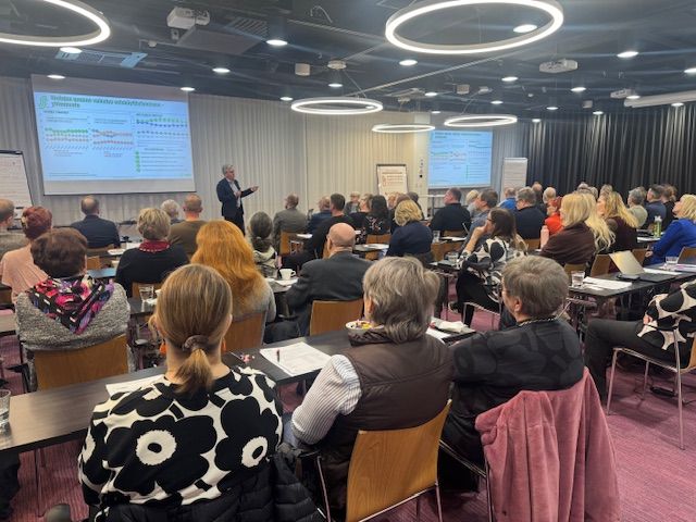 Ryhmä ihmisiä kokoushuoneessa kuuntelemassa esitelmää.