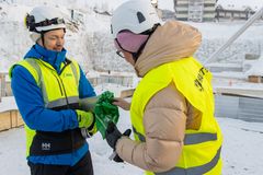 Kaksi henkilöä kypärissä ja heijastinliiveissä lumisella rakennustyömaalla.