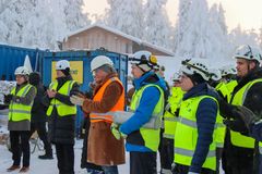 Ryhmä ihmisiä kypärissä ja huomioliiveissä seisoo lumisessa ulkotilassa.