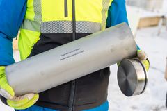 Henkilö pitelee teräksistä säiliötä, jonka päällä on kaiverrettu teksti.