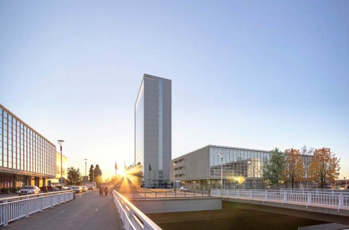 Kuva valoisasta arkkitehtuurimaisemasta, jossa näkyy moderneja rakennuksia ja silta.