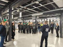 Ryhmä ihmisiä kuuntelee puhetta suuressa rakennuksessa.