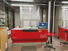 Punainen automatisoitu kone huoneessa, jossa on tietokone ja lisäpöytä.