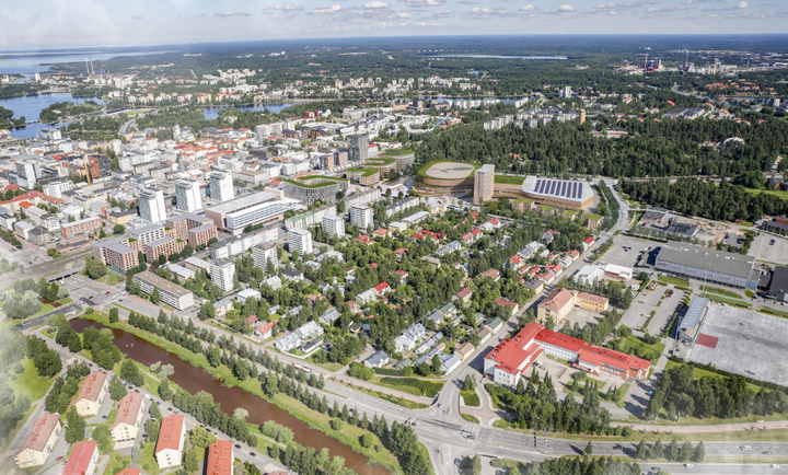 Ilmakuva vihreästä kaupunkialueesta, jossa on sekä korkeita rakennuksia että matalia omakotitaloja, metsää taustalla.