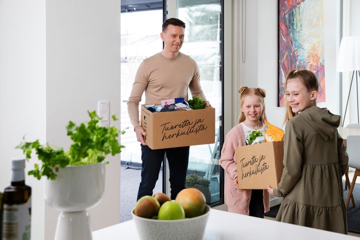 Mies ja kaksi lasta kantavat ruoan verkkokaupan uokaostoksia kodin keittiöön.