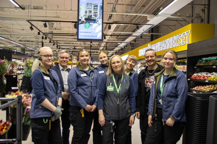 Ryhmä ihmisiä poseeraa ruokakaupassa.