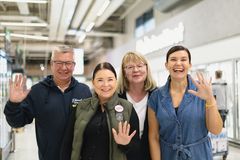 Neljän iloisesti hymyilevän henkilön ryhmä sisätiloissa, kaikki heiluttavat kättään kameralle.