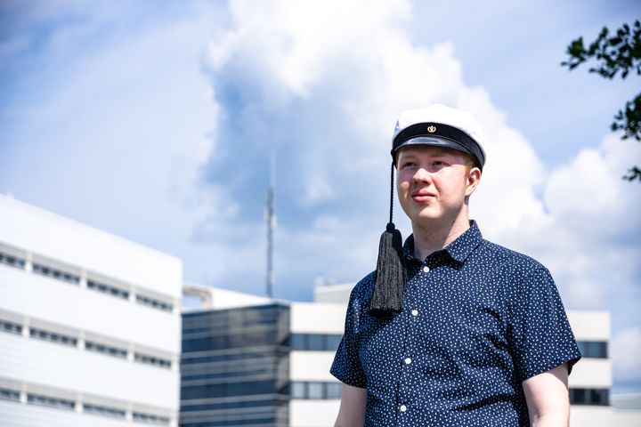 Kuvassa Joose Sippola katsoo kesäiselle taivaalle Mattilanniemen rannassa päässään teekkarilakki.