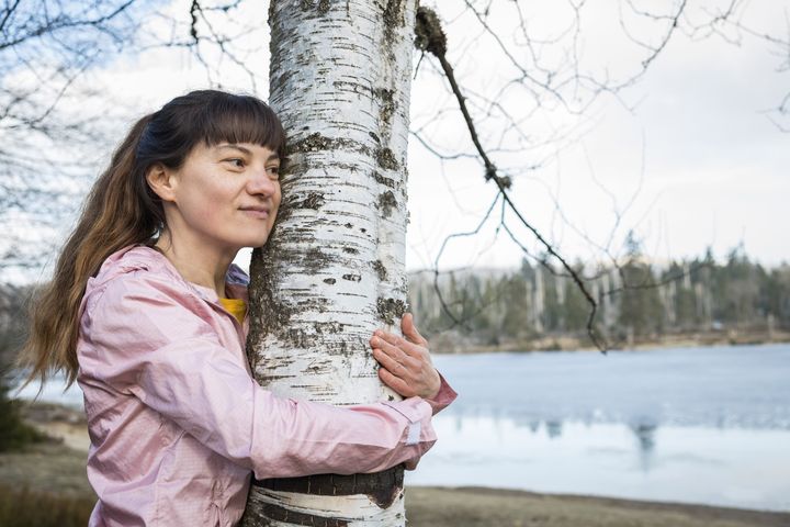 Henkilö hymyilee ja halaa puuta