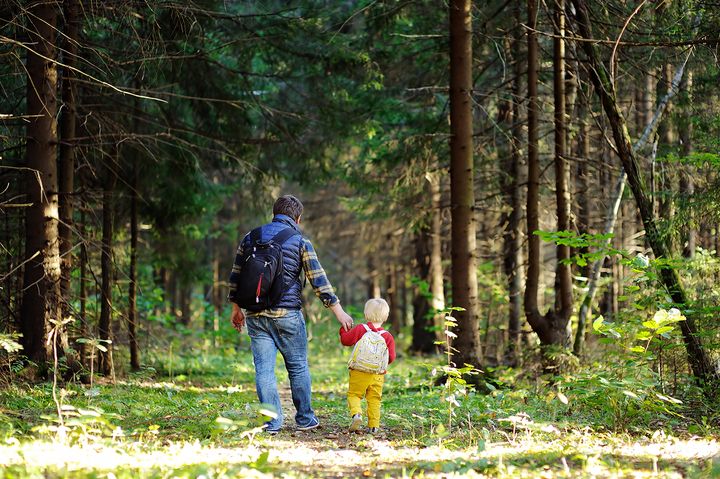 Mies ja lapsi kävelevät käsikkäin metsäpolulla.