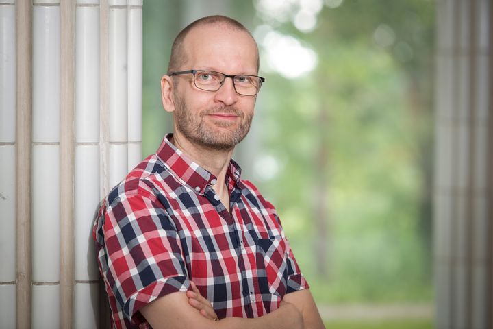 Mies seisoo puistossa, pukeutuneena ruudulliseen paitaan.