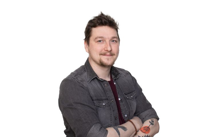 Ville Tikka seisomassa hymyillen, kädet ristissä. Valkoinen tausta.