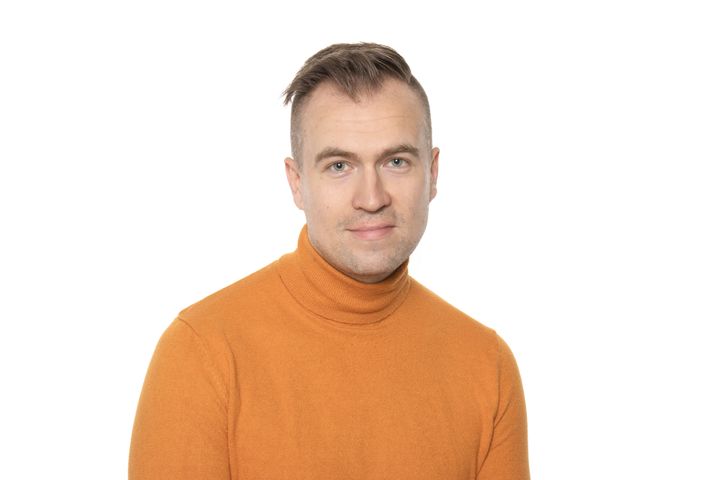 Mies keltaisessa kauluspoolossa katsoo kameraan. Valkoinen tausta.