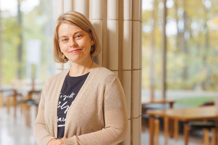 Henkilö nojaa tolppaan ja katsoo hymyillen kameraan.
