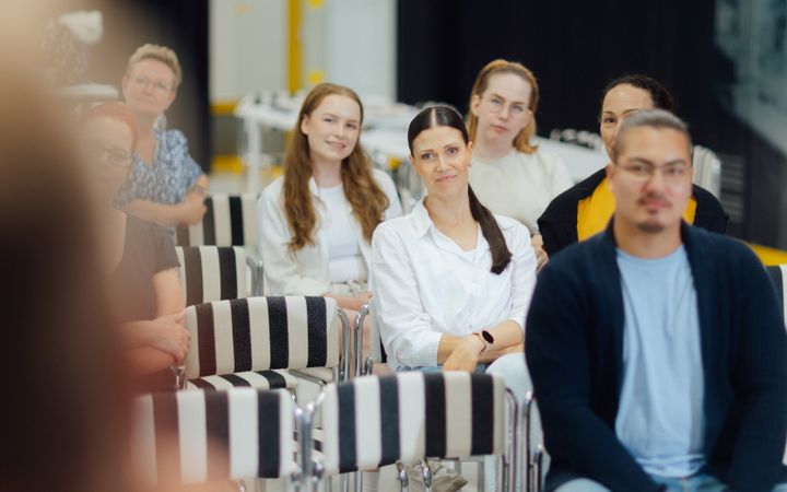 Ryhmä ihmisiä istuu sisätiloissa tapahtumassa kuulemassa puhujaa.