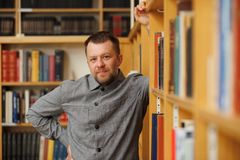 Henkilö nojaa kirjahyllyyn ja katsoo hymyillen kameraan.