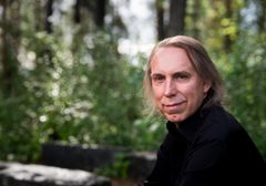 Henkilö on ulkona ja katsoo kameraan. Musta paita.