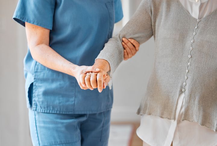 Hoitaja tukee iäkästä henkilöä käsivarresta. Kuvassa näkyvät vain kädet ja vartalo.