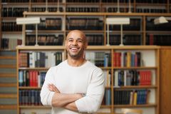 Henkilö seisoo kirjastossa yllään valkoinen pikähihainen paita. Kädet ovat ristittynä ja taustalla näkyy kirjahylly ja kirjoja.