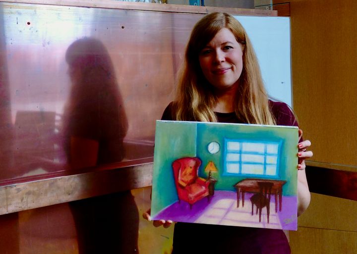 Henkilö pitää käsissään maalausta, jossa näkyy nojatuoli ja pulpetti.