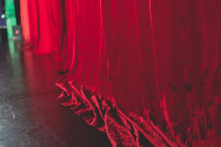 Punainen samettiverho lavalla. Vasemmassa alakulmassa näkyy lavan lattiaa.