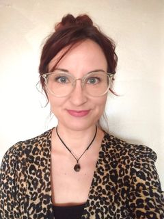 Henkilöllä on silmälasit ja leopardikuosinen vaate. Hän hymyilee kameralle.