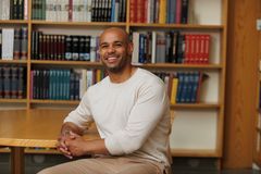 Kuvassa henkilö istuu kirjahyllyn edessä ja hymyilee.