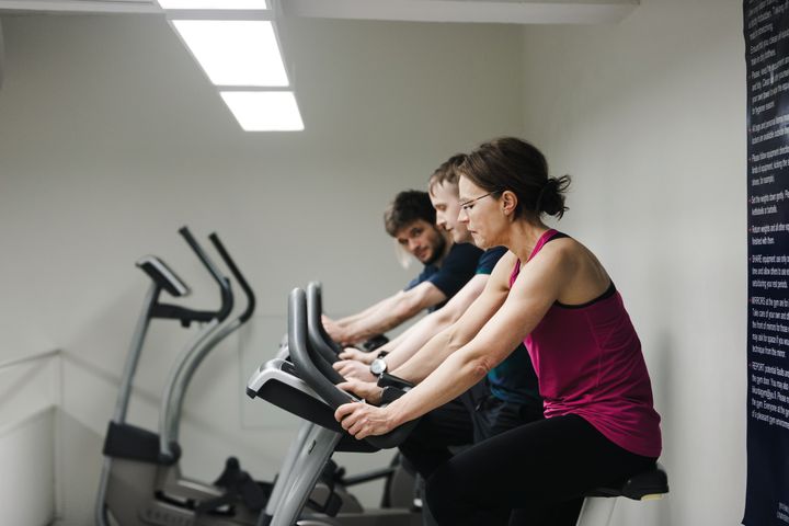 Kuntopyöräilijöitä rivissä kuntosalilla. Etualalla henkilö purppuranvärisessä urheilutopissa.