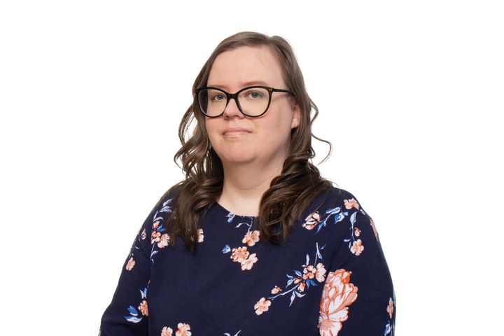 Henkilö hymyilee kameralle. Kukkakuvioinen paita ja silmälasit.